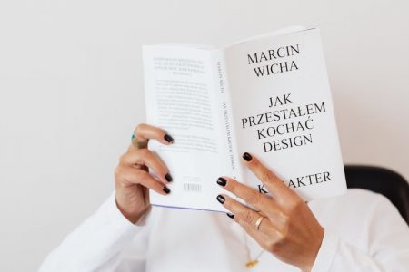 Anonymous female in white shirt with gold chain on neck reading interesting book covering face while sitting on black chair