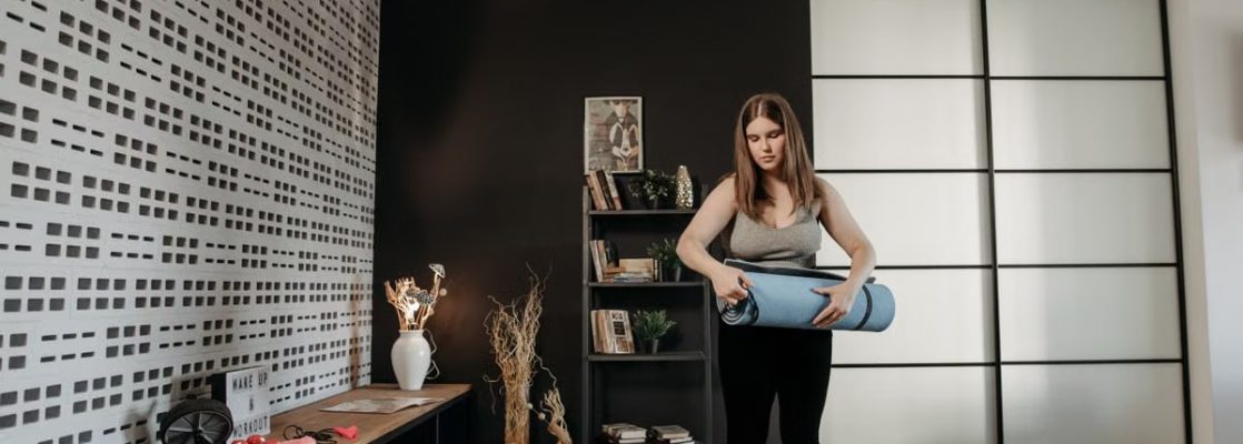Plus size woman rolling a yoga mat in a stylish indoor setting with modern decor.