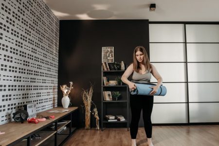 Plus size woman rolling a yoga mat in a stylish indoor setting with modern decor.